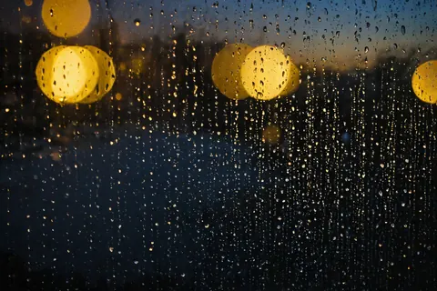 Raindrops on glass with blurred golden lights in the background