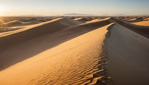 Sunrise over vast golden sand dunes with distant mountains on the horizon